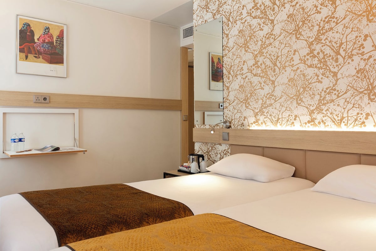 Een hotelkamer met twee bedden, een nachtkastje met koffiezetapparaat, een spiegel en kunst aan de muren.