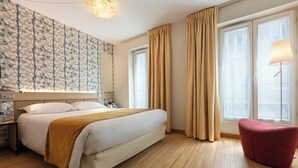 Une chambre d’hôtel avec un grand lit, une table de chevet, une chaise rouge et une fenêtre avec des rideaux.