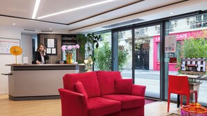 Un hall d’hôtel avec un canapé rouge, un comptoir d’accueil et une vue sur la rue.