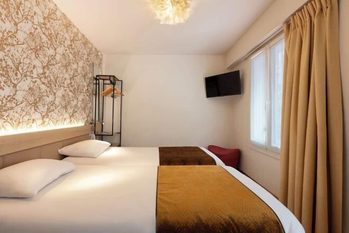 Een hotelkamer met twee bedden, een aan de muur bevestigde televisie en een raam met gordijnen.
