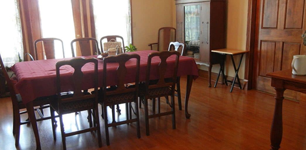 A dining area with a wooden table and chairs, a red tablecloth, and a cabinet.