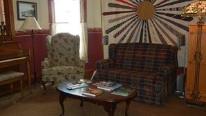 Una sala de estar acogedora con un piano, un sillón floral, un sofá escocés y una mesa con libros.