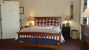 A bedroom with a wooden bed, two bedside lamps, a dresser, a chair, and a door.