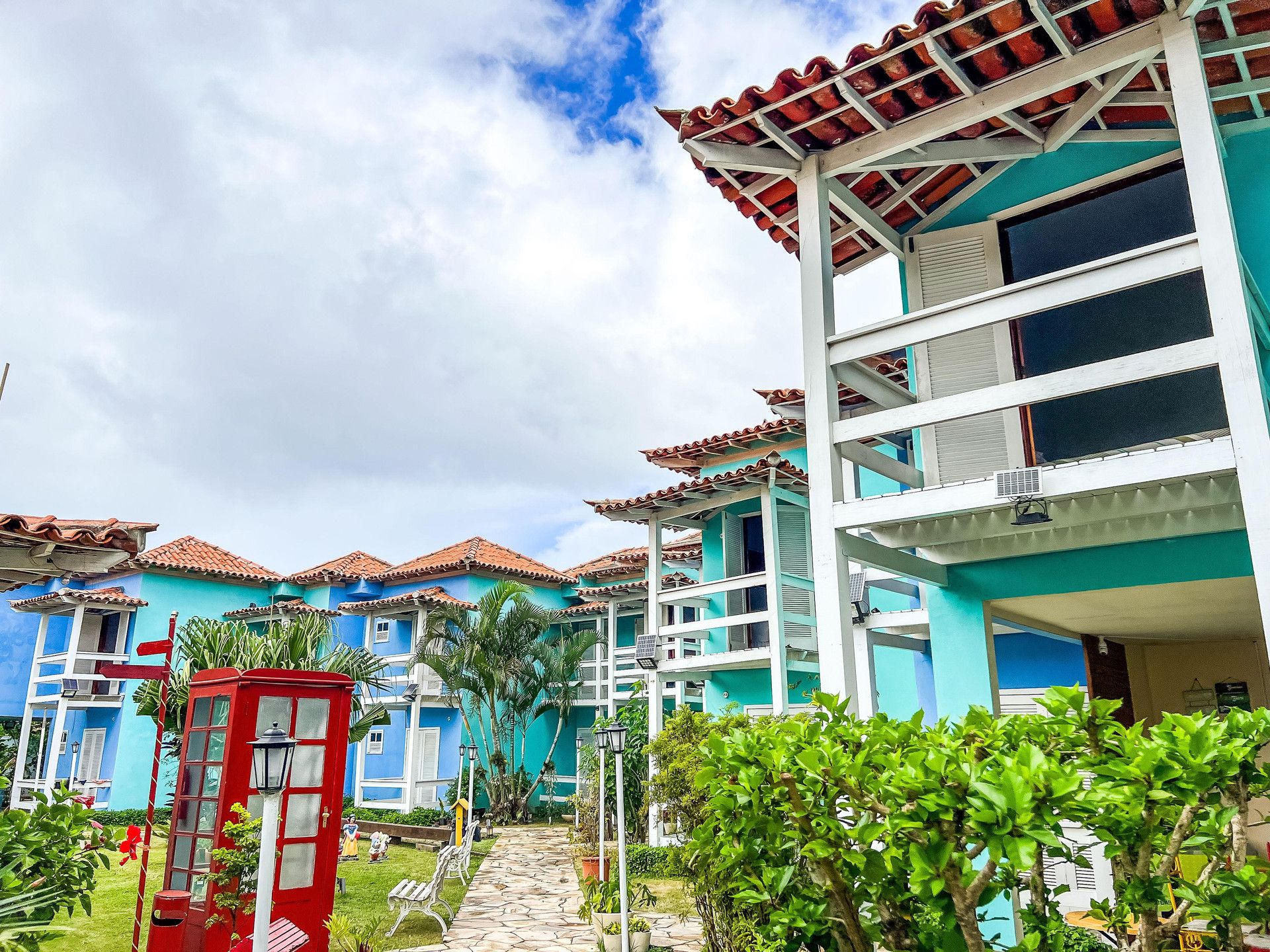Um hotel com edifícios de vários andares, uma cabine telefônica vermelha e um jardim bem cuidado com caminhos.