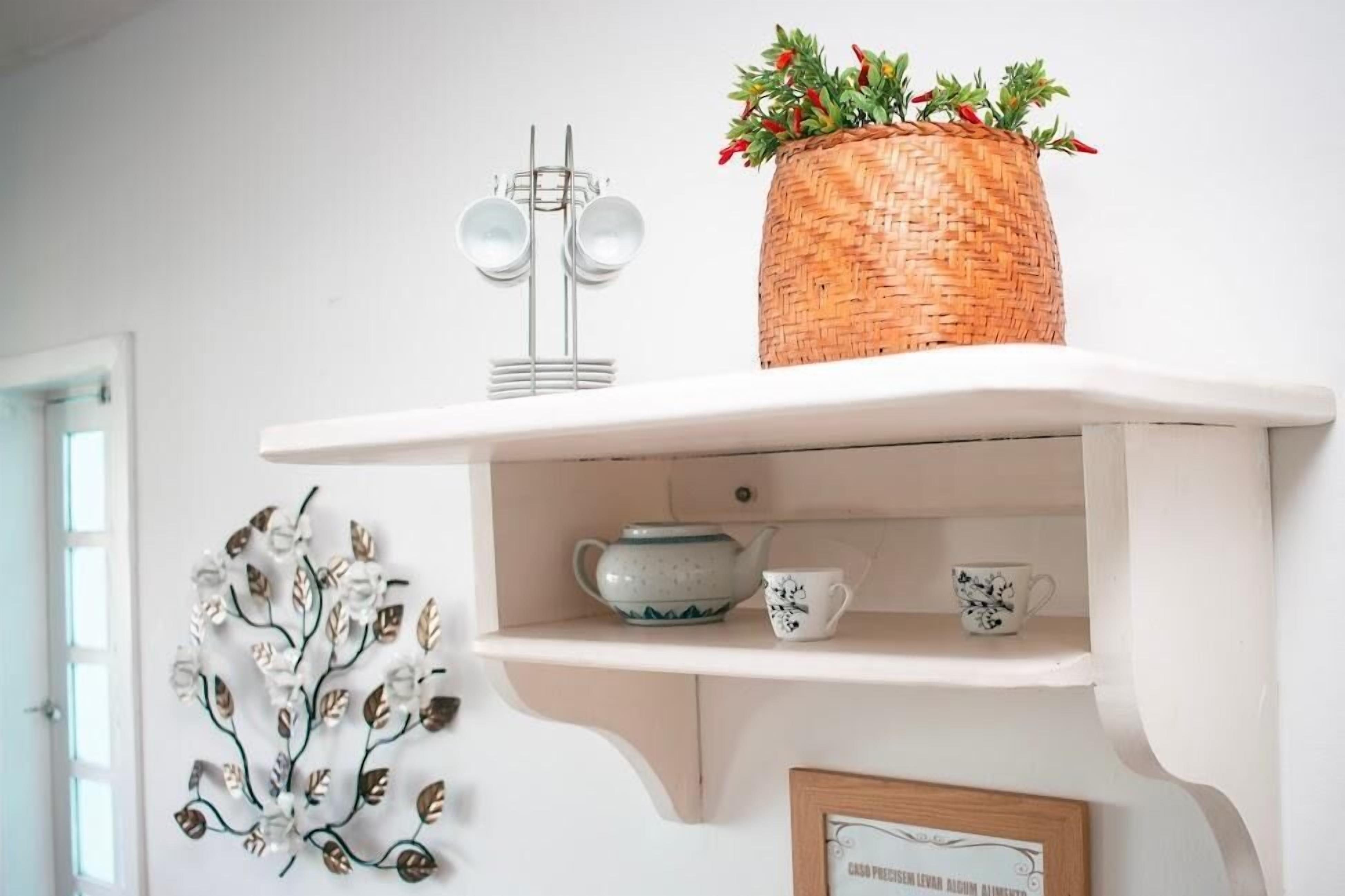 A white shelf with a woven basket containing red flowers, a teapot, and two cups.