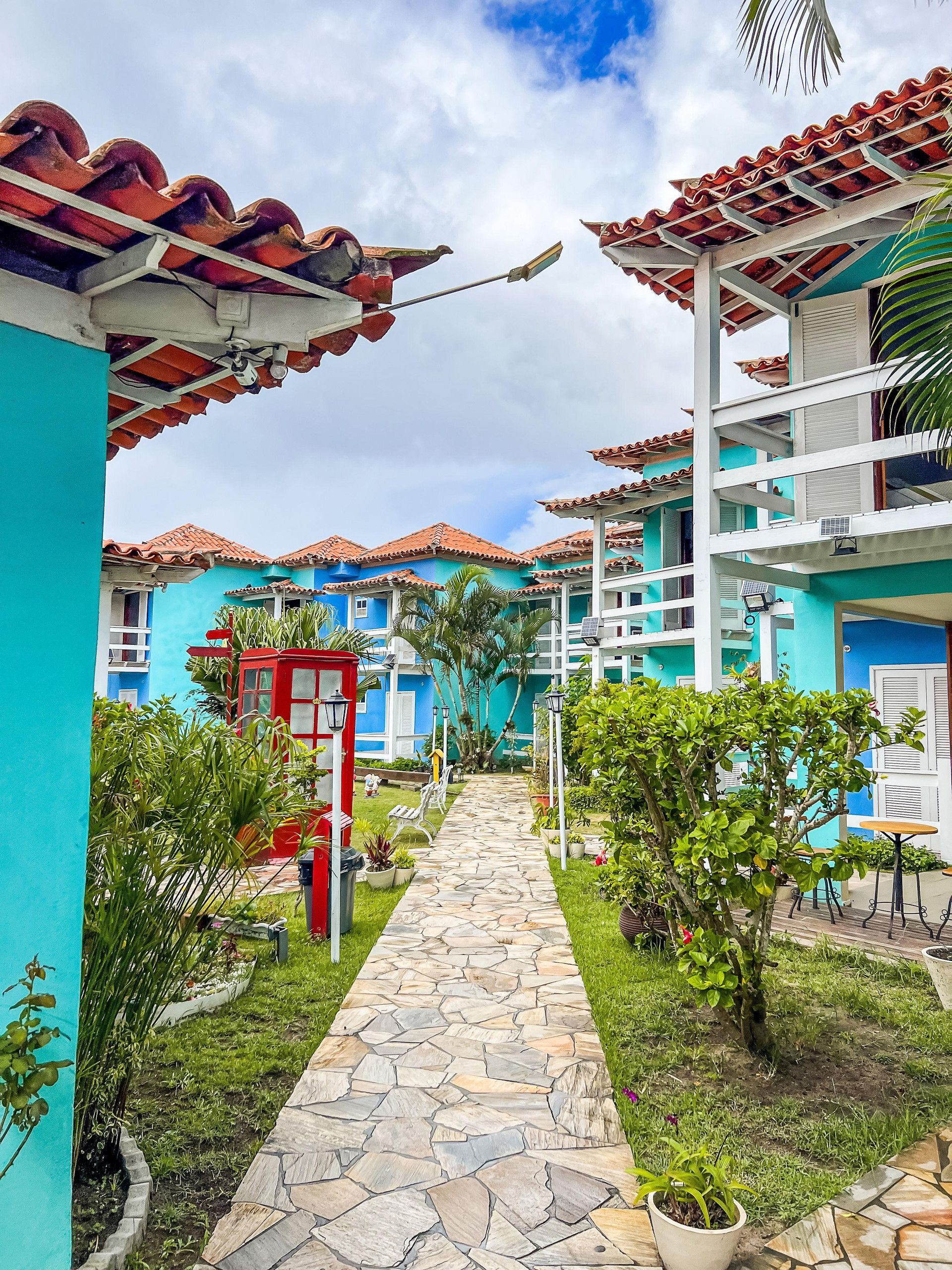 Uma trilha leva a um edifício com telhado ladrilhado e fachada azul.
