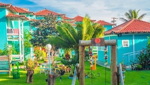 Um pátio colorido com balanço, palmeiras e um edifício com telhados de telha vermelha.