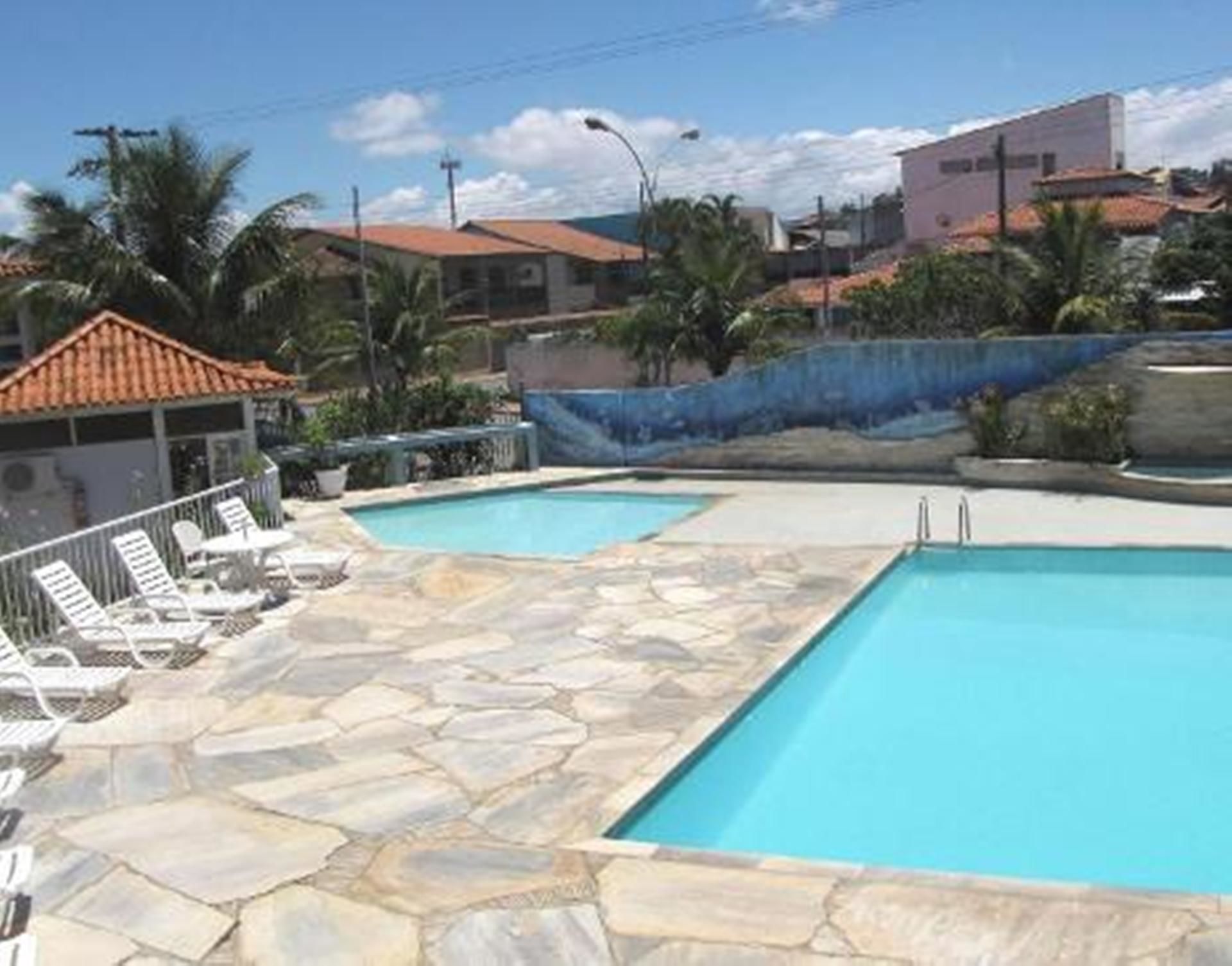 A swimming pool with stone tiles and lounge chairs, surrounded by buildings and palm trees.