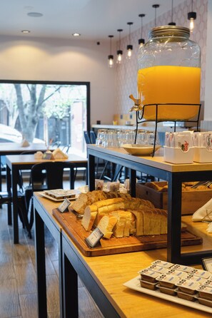A breakfast buffet with bread, pastries, and a large glass jar of orange juice. - Hotel Bariloche By Tierra Gaucha (San Carlos de Bariloche)