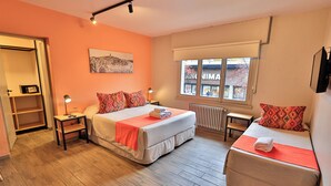 A hotel room with two beds, a window with a view of a building, a radiator, and a shelf with a clock. - Hotel Bariloche By Tierra Gaucha (San Carlos de Bariloche)