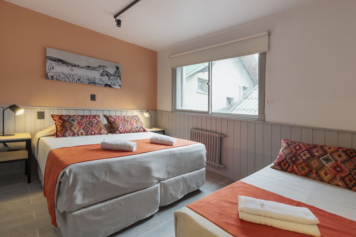 A double room with two beds, a window, a radiator, and a painting on the wall.