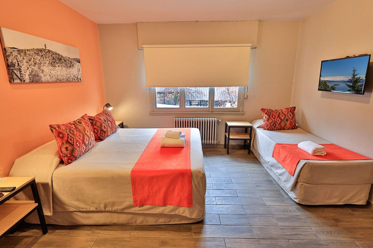 Une chambre d’hôtel avec deux lits, un bureau, une chaise, un radiateur et une fenêtre donnant sur un beau paysage.