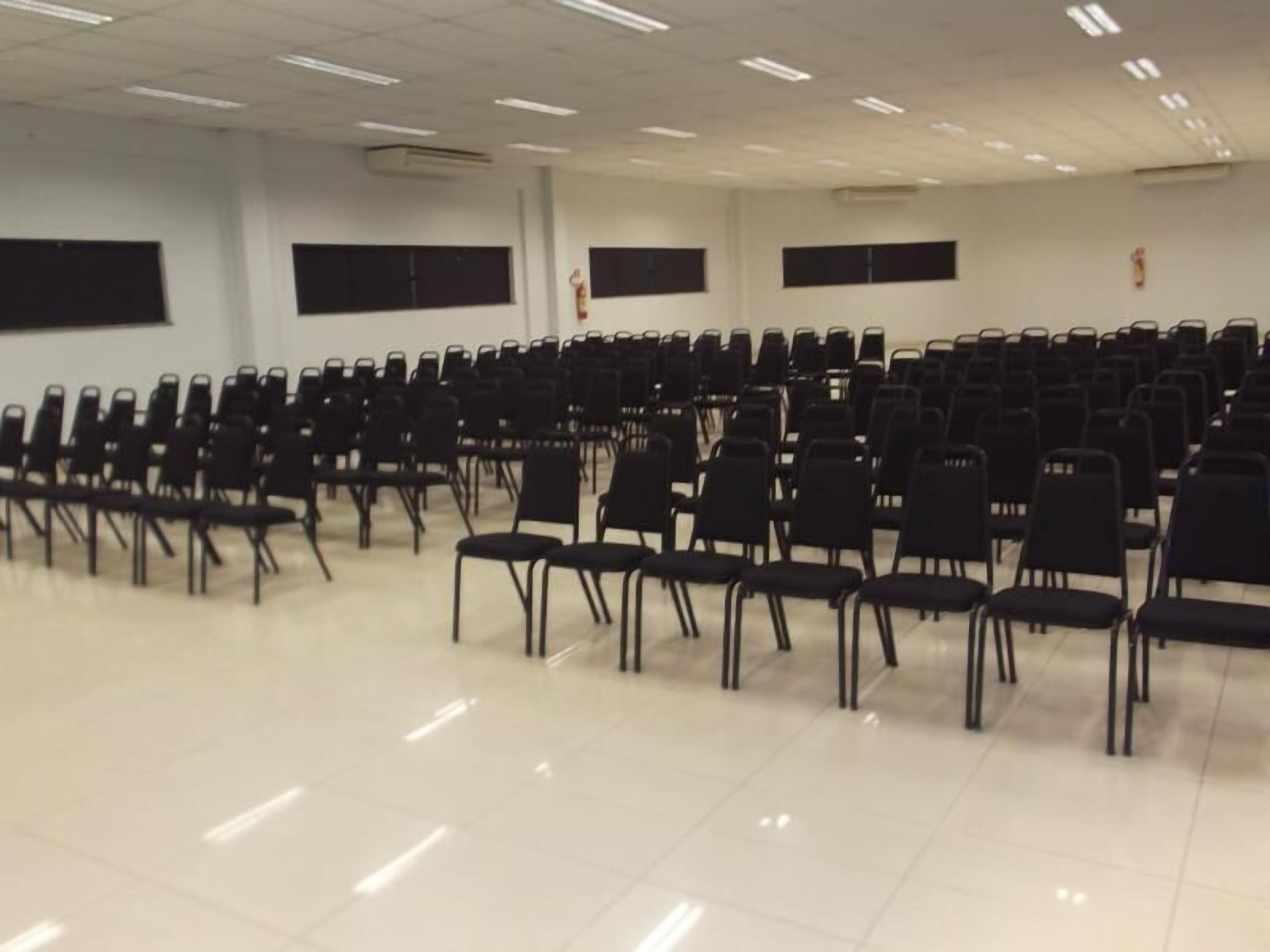 A conference room with rows of black chairs, white walls, and ceiling lights.