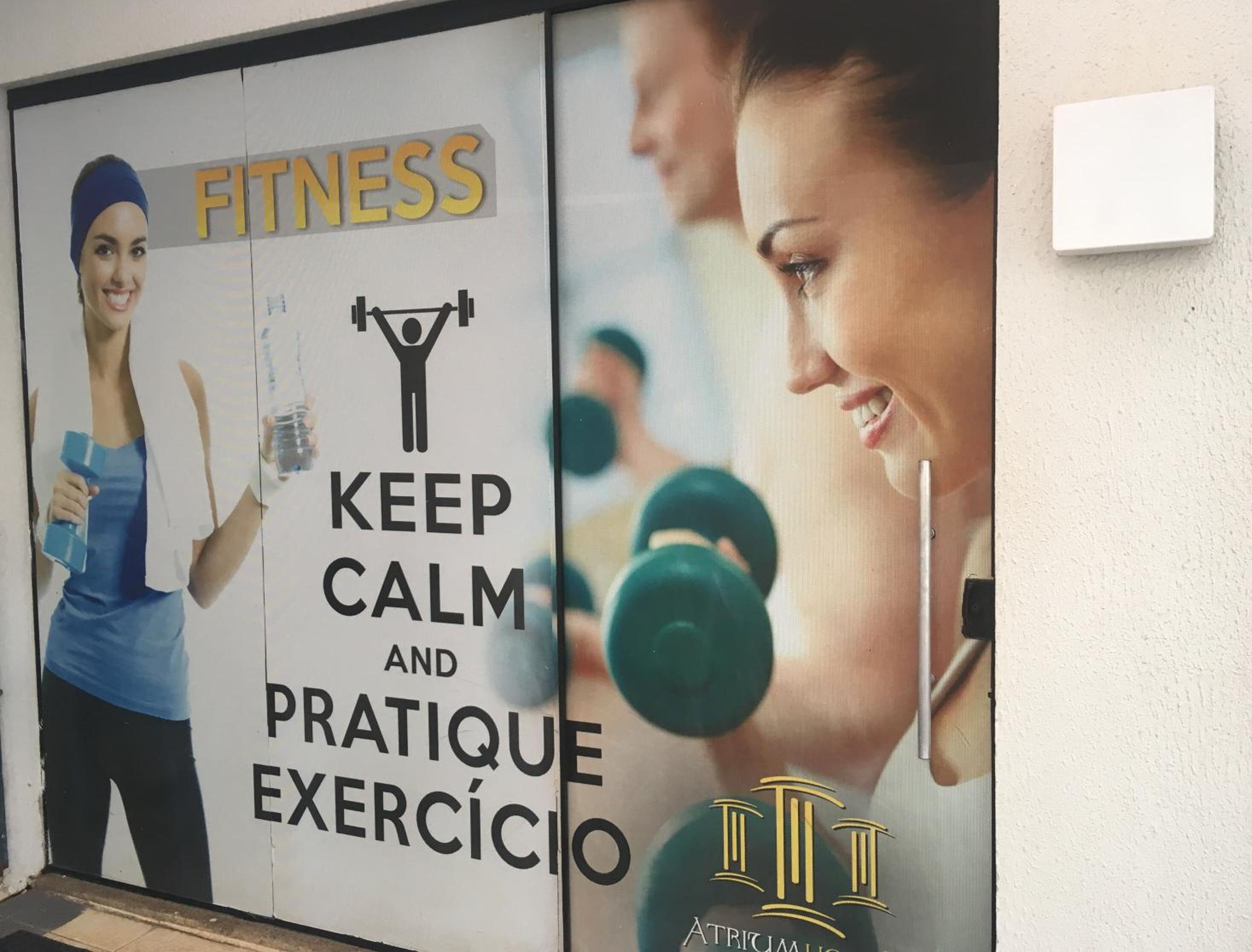A gym wall with a poster encouraging to "KEEP CALM AND PRATIQUE EXERCÍCIO" and a logo for "ATRÍCIMA".