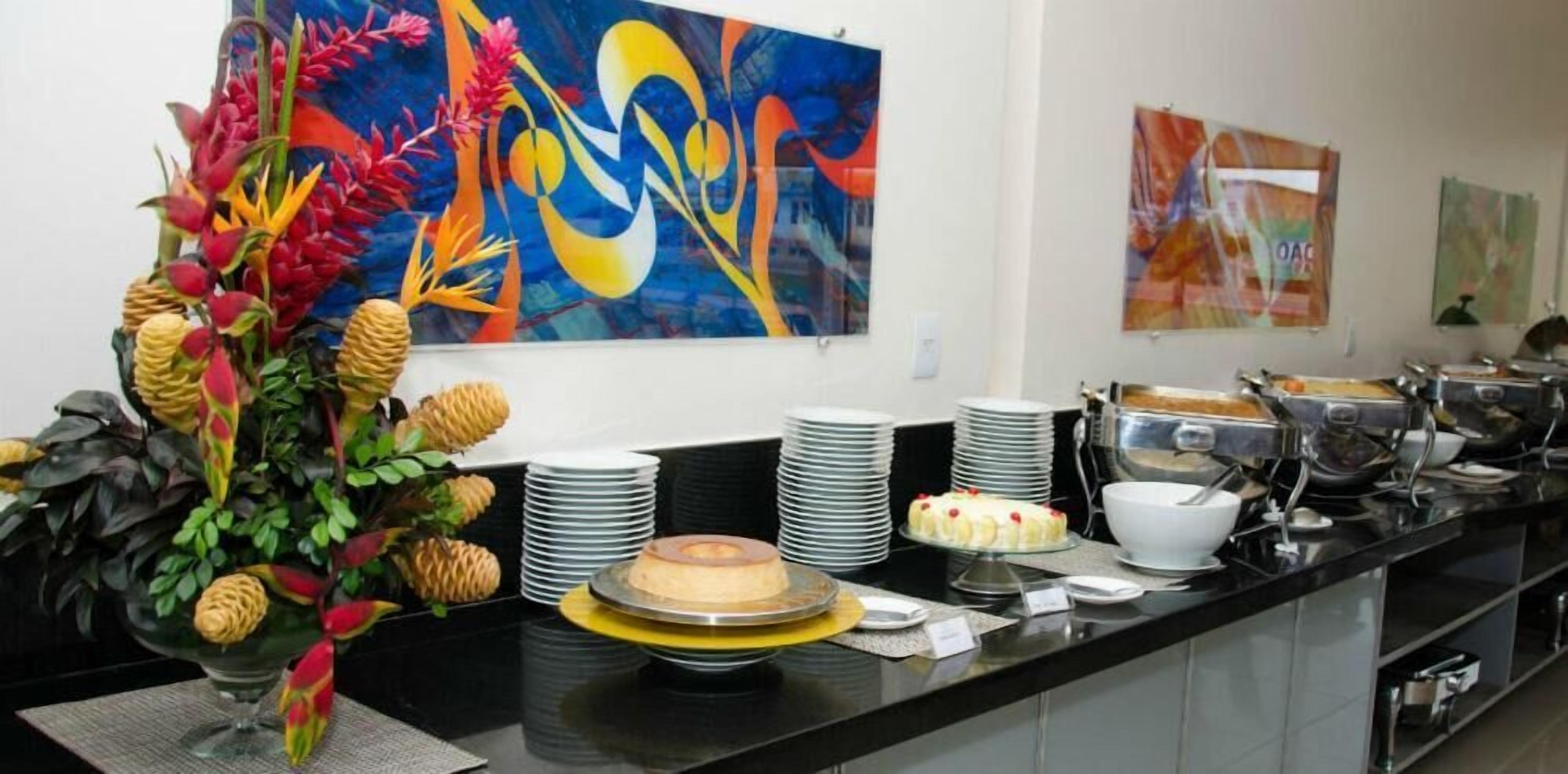 A buffet setup with a variety of dishes, including a cake on a yellow stand, and a large abstract painting on the wall.