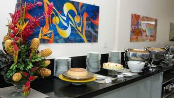 A buffet setup with a variety of dishes, including a cake on a yellow stand, and a large abstract painting on the wall.