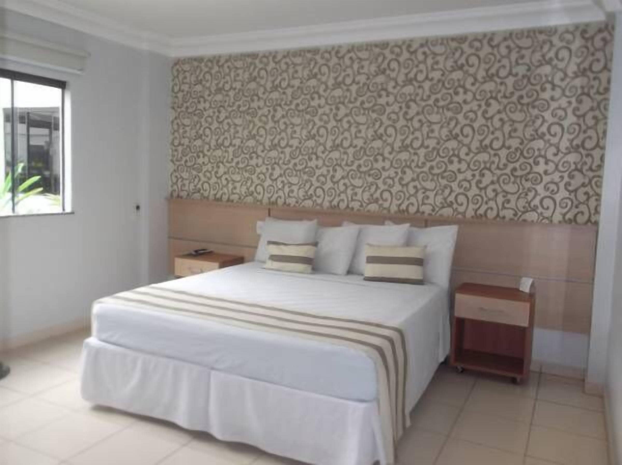 A bedroom with a large bed, a nightstand, a bedside table, and a patterned wallpaper.