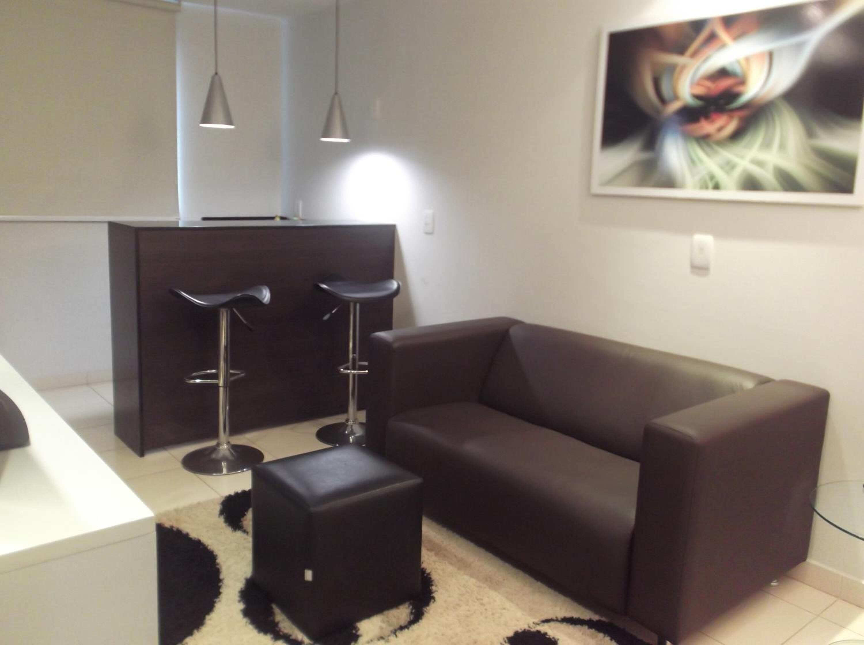 Una sala de estar moderna con un sofá marrón oscuro, dos taburetes negros, una mesa de centro de vidrio y un cuadro en la pared.
