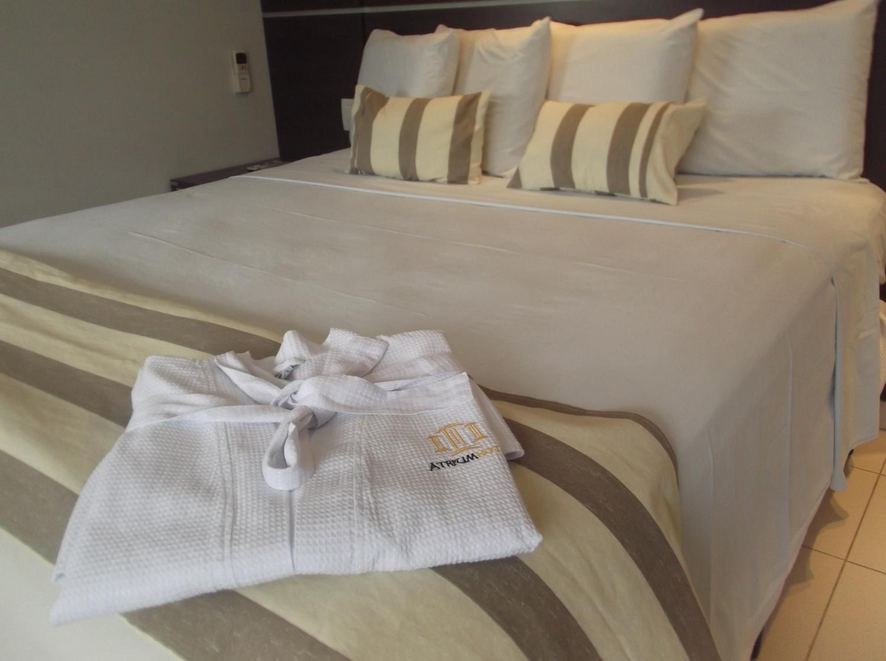 A neatly made bed with a striped pillow set and a white bathrobe on the bed.