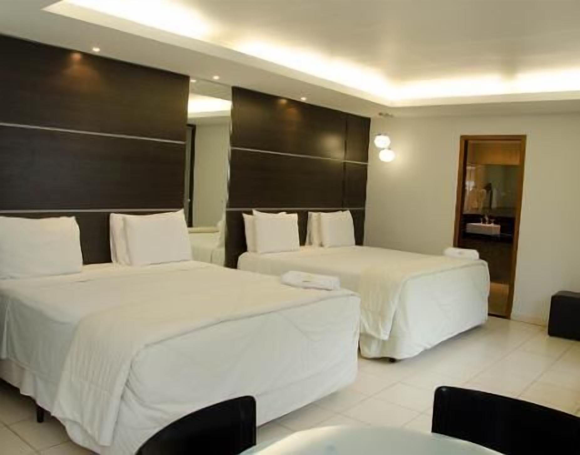 A hotel room with two beds, a large mirror, and a small bathroom.