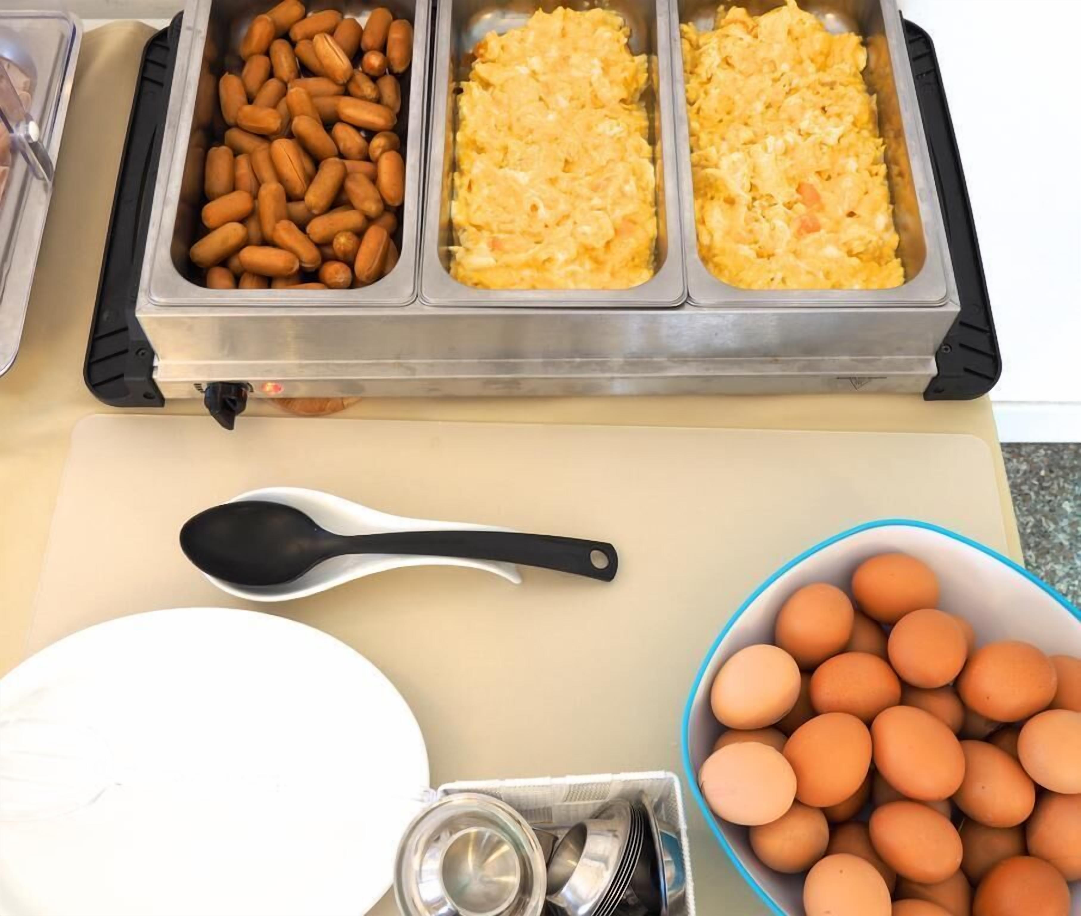 Montaje de bufé con recipientes de comida, un tazón de huevos y una cuchara sobre una mesa.