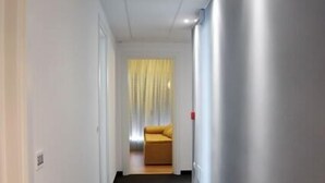A narrow hallway with a black carpet leading to a room with a yellow bed and a window with yellow curtains. - Hotel Dante (Jesolo)