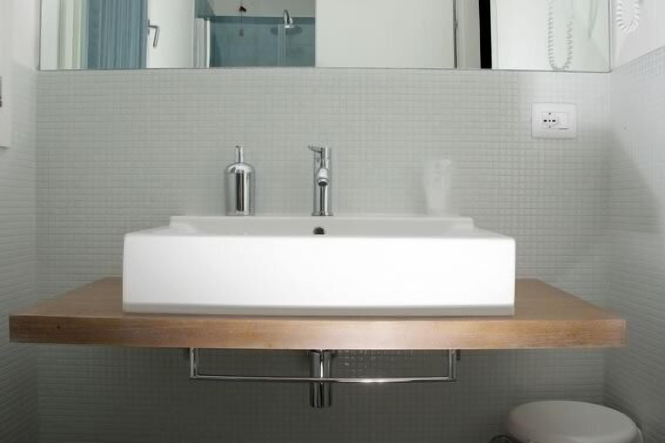 Un bagno con un lavandino bianco, un piano d'appoggio in legno e uno specchio sopra.