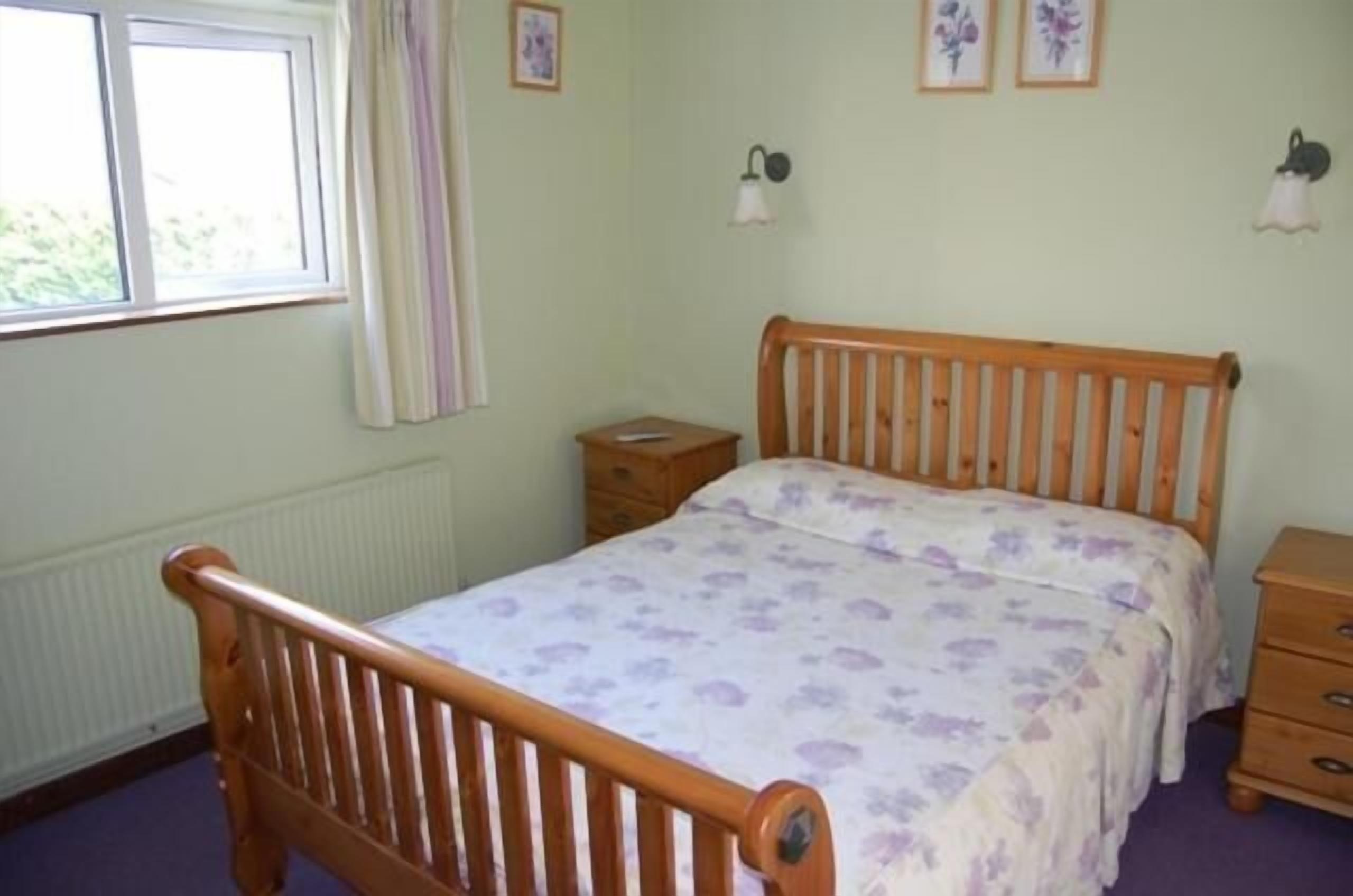 A bedroom with a wooden bed, a bedside table, a dresser, and a window with curtains.