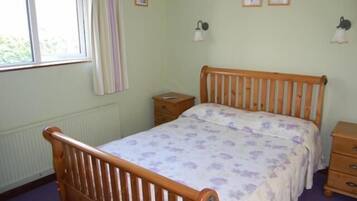 A bedroom with a wooden bed, a bedside table, a dresser, and a window with curtains.