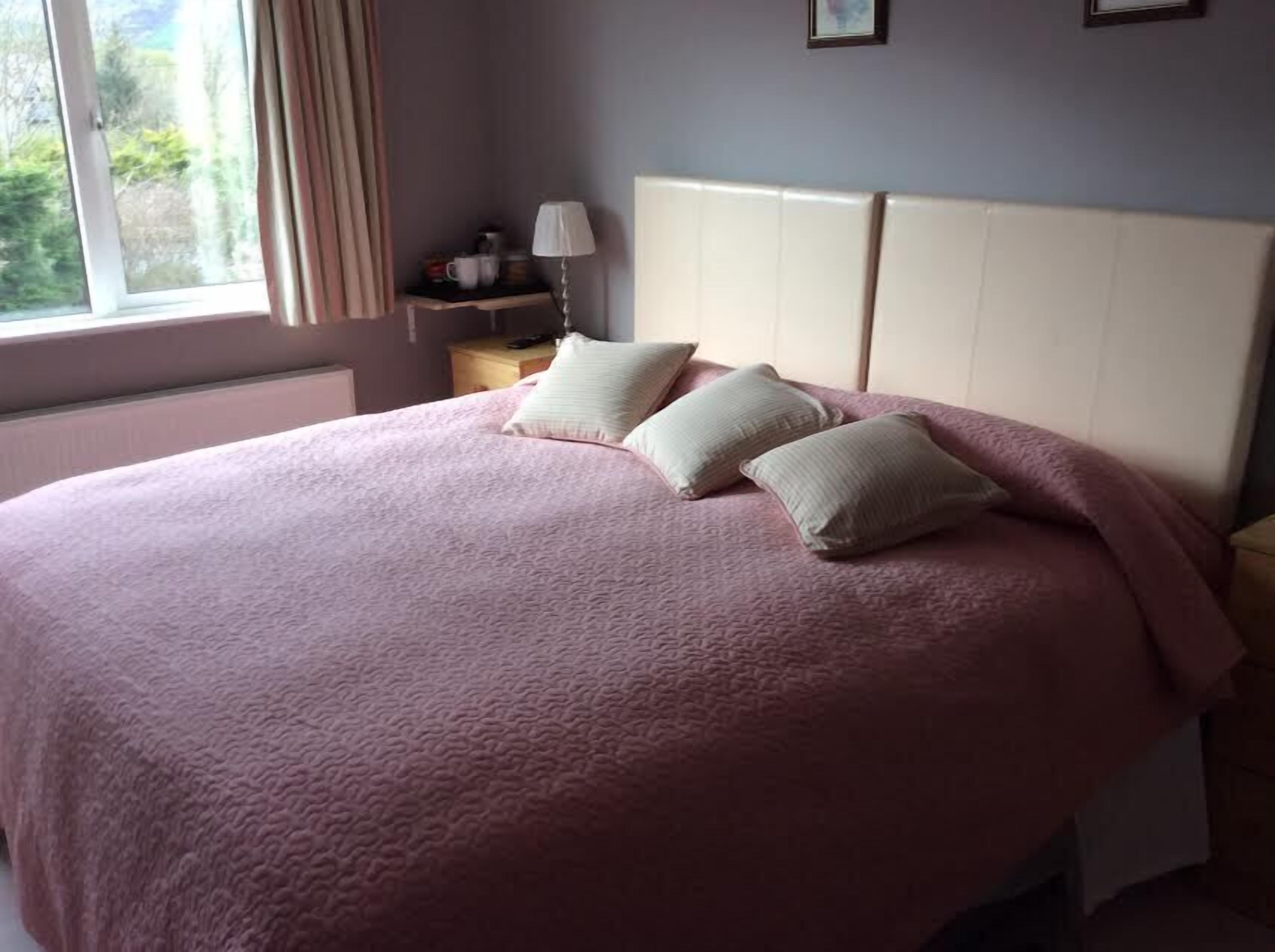 A bedroom with a large bed, a nightstand, a lamp, and a window with curtains.