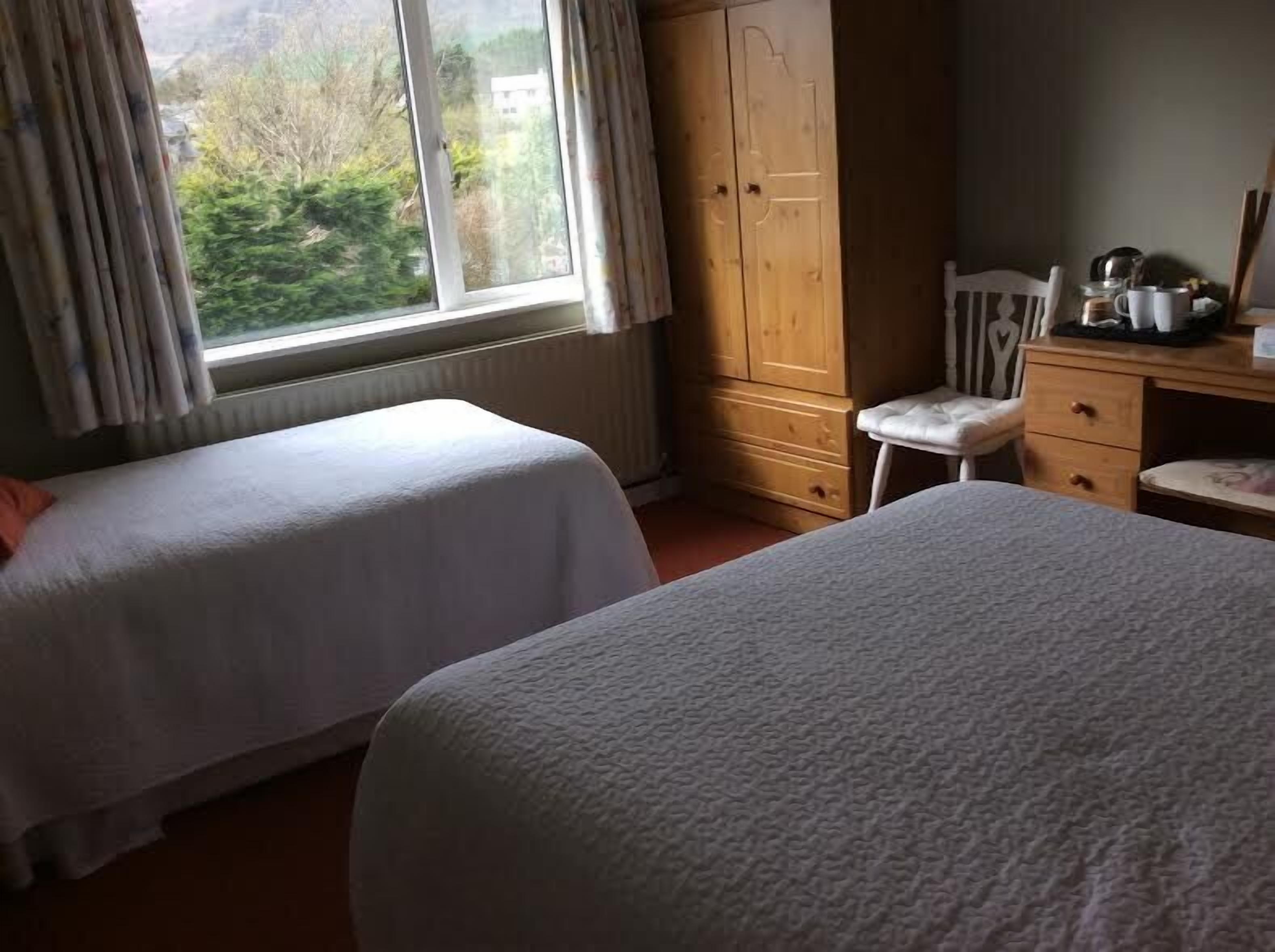 Ein Schlafzimmer mit zwei Betten, einem Holzschrank, einem Schreibtisch mit Stuhl und Blick ins Grüne.