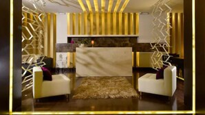 A modern lobby with a reception desk, two white armchairs, a patterned rug, and geometric wall decorations.