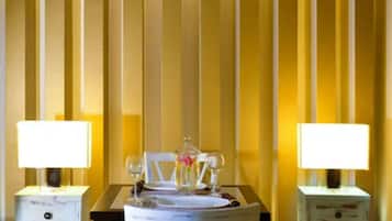 A dining area with a table set for two, flanked by two bedside tables with lamps, against a striped wall.