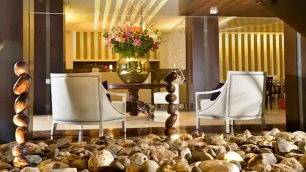 A lobby with a stone floor, two white chairs, a central table with a vase of flowers, and a modern interior design.