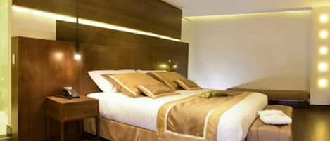 Una habitación de hotel moderna con una cama grande, una mesita de noche y una mesita auxiliar.