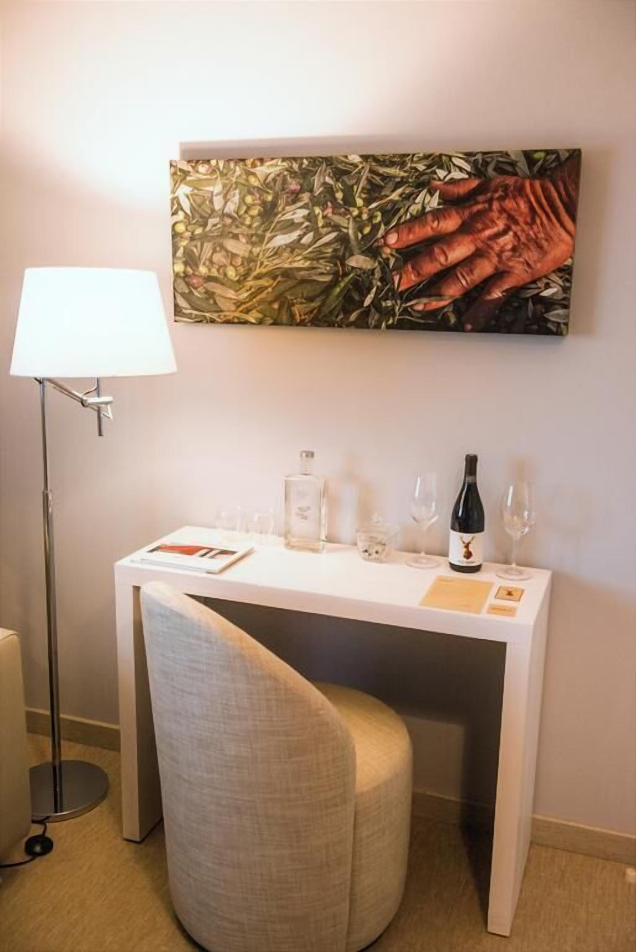 A small, neatly arranged desk with a chair, a lamp, and a wine bottle and glasses on it.