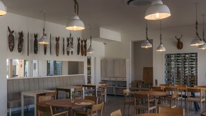 A spacious dining area with multiple wooden tables and chairs, pendant lighting, and wall-mounted animal head decorations. - Herdade da Rocha Boutique Lodge (Crato)