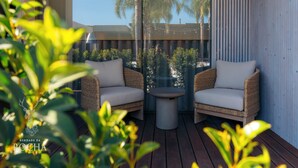 A balcony with wicker furniture and a small table, overlooking a pool and palm trees. - Herdade da Rocha Boutique Lodge (Crato)