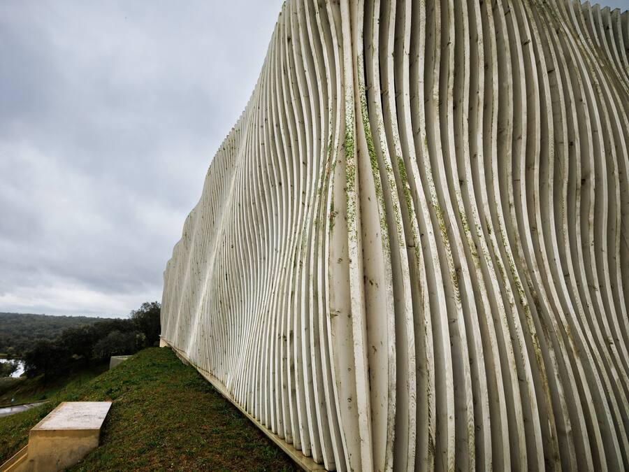 Una estructura grande y blanca con costillas, base plana, rodeada de césped y un cielo nublado.
