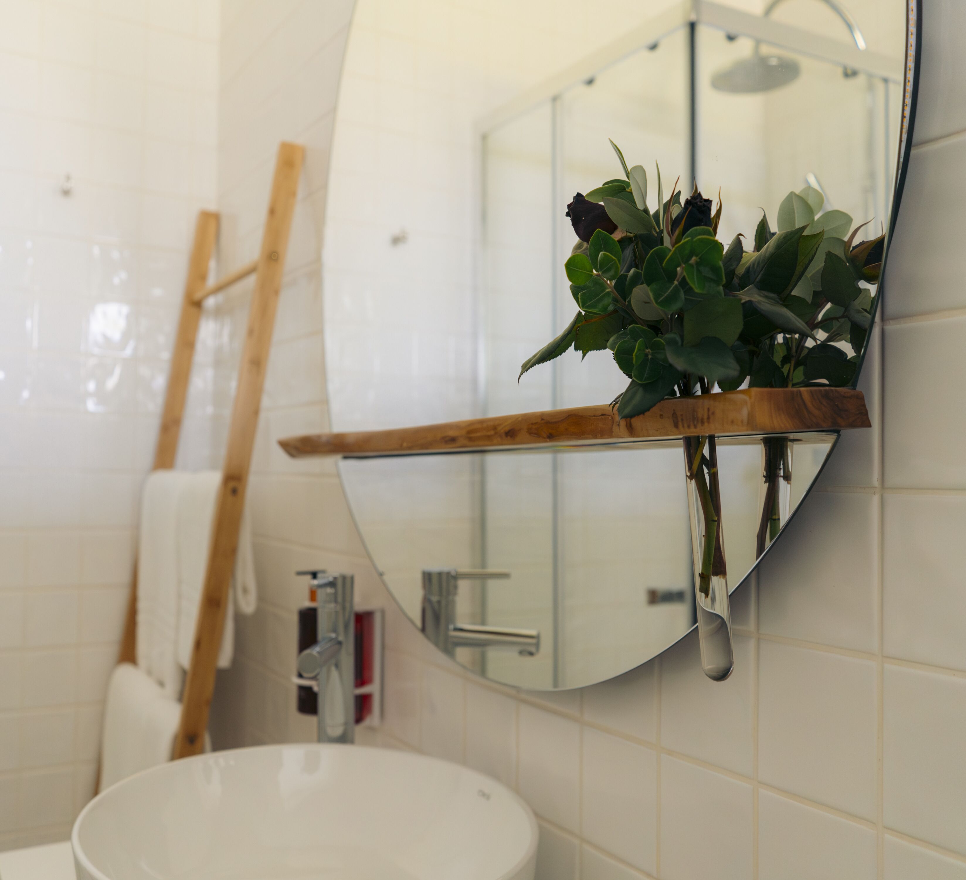 A bathroom with a white sink, a wooden shelf with a plant, a mirror, and a shower.