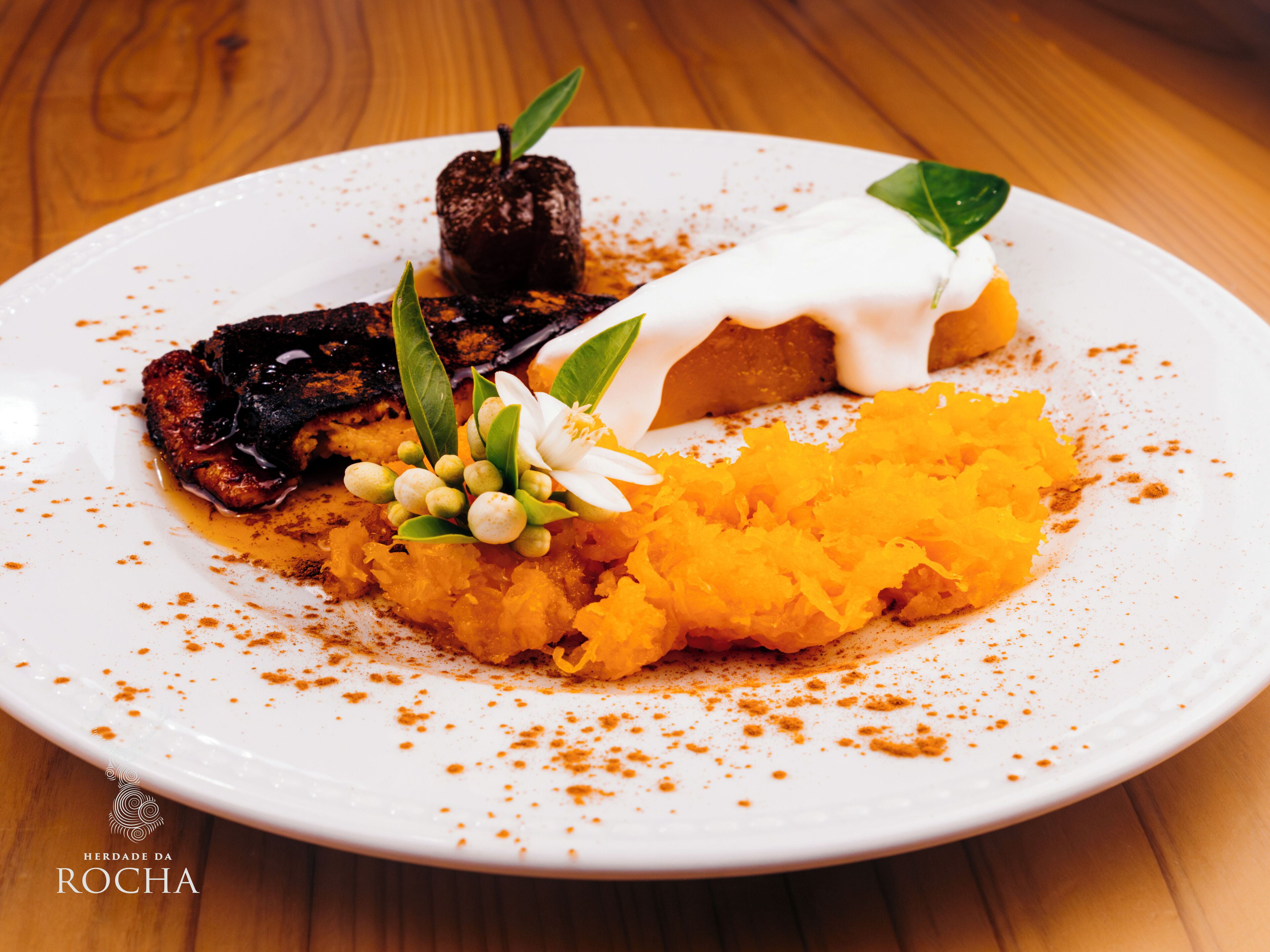 Un plato de comida con varios platos, incluyendo un trozo de carne, un producto horneado y un puré de verduras, adornado con hierbas y especias.