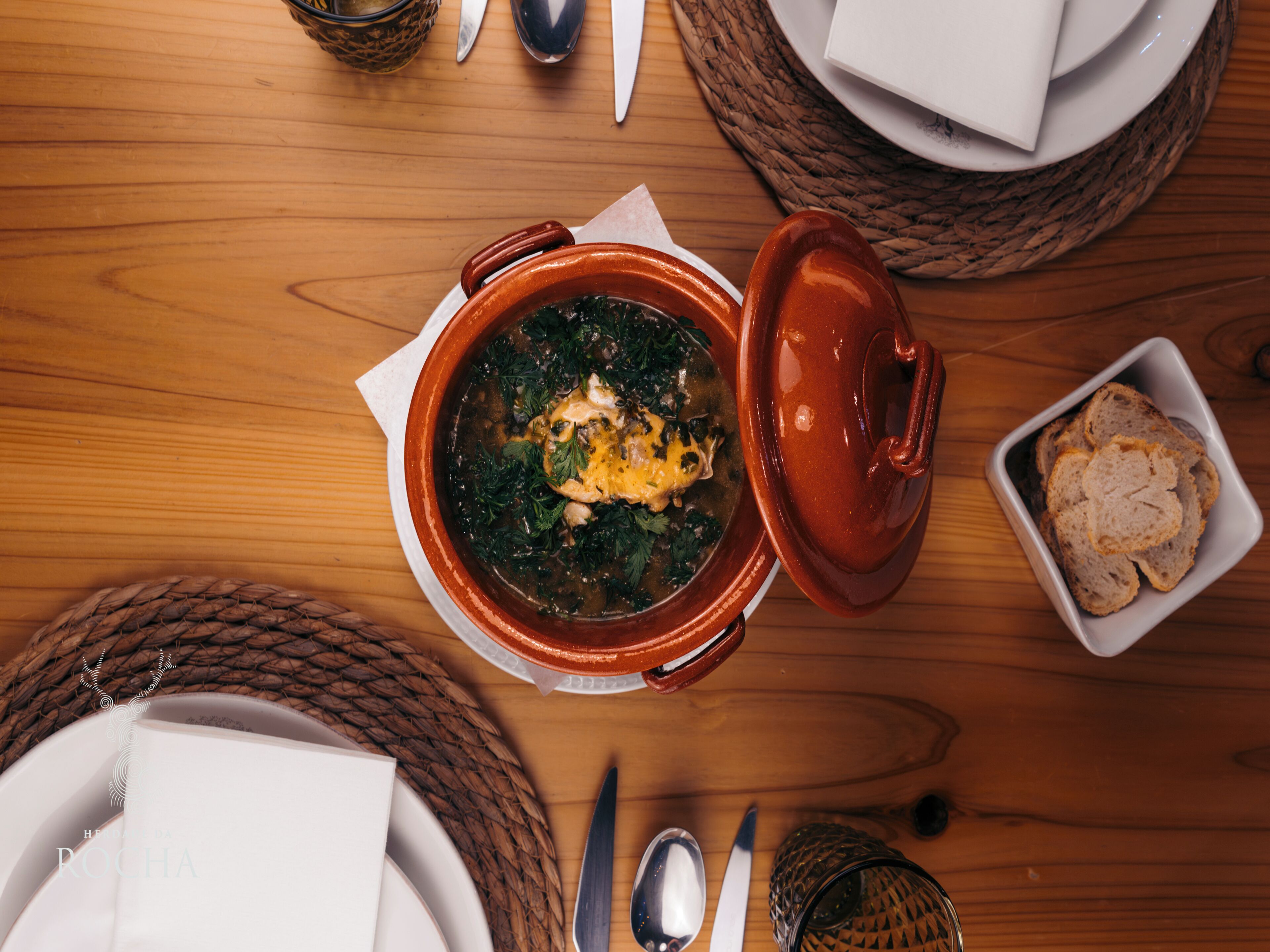 A wooden table with a bowl of soup, a plate of bread, and a woven basket.