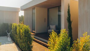 A modern, minimalist house with a wooden deck, a glass door leading to a living area, and a small garden with shrubs. - Herdade da Rocha Boutique Lodge (Crato)