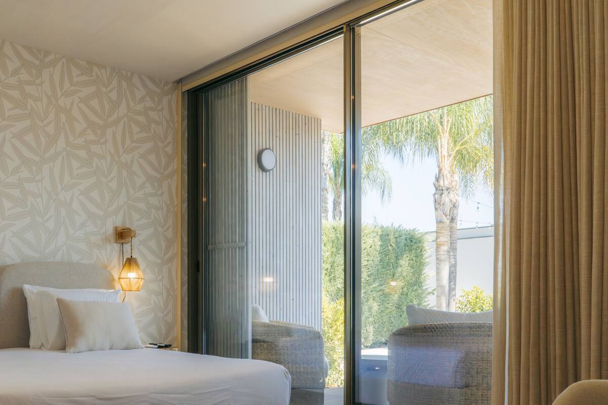 A bedroom with a large bed, two bedside lamps, and a view of the outdoors through a sliding glass door.