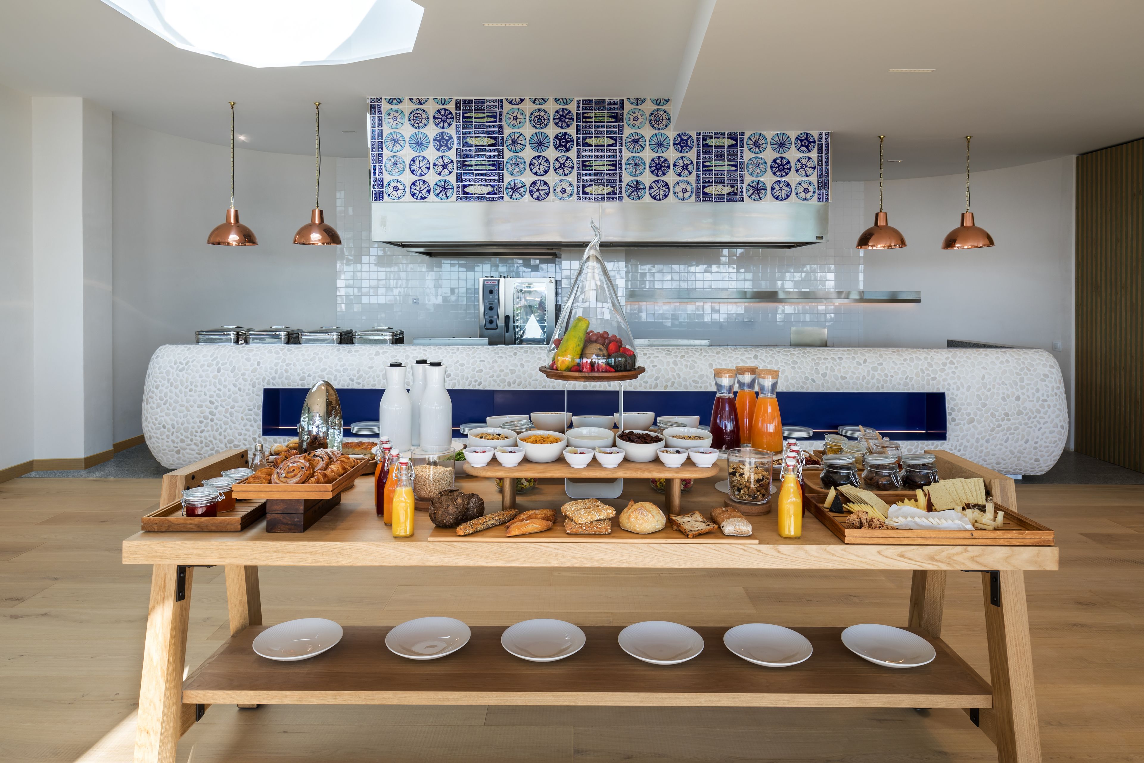 Una mesa de madera con una barra de desayuno, que incluye diversos alimentos y aderezos, con una cocina al fondo.