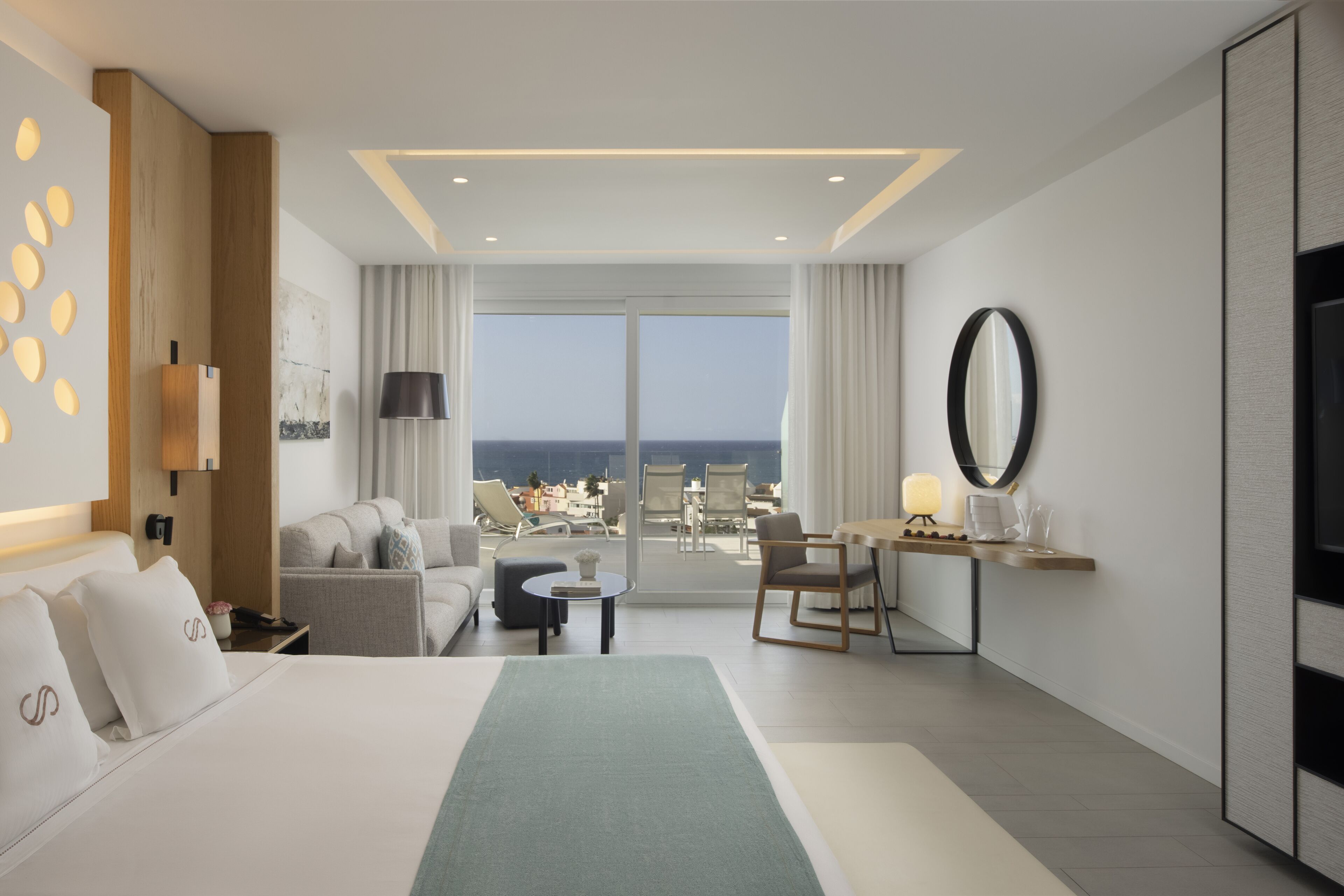 A modern hotel room with a large bed, a desk, a chair, and a view of the ocean.
