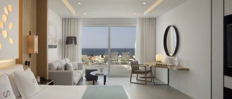 A modern hotel room with a large bed, a desk, a chair, and a view of the ocean.