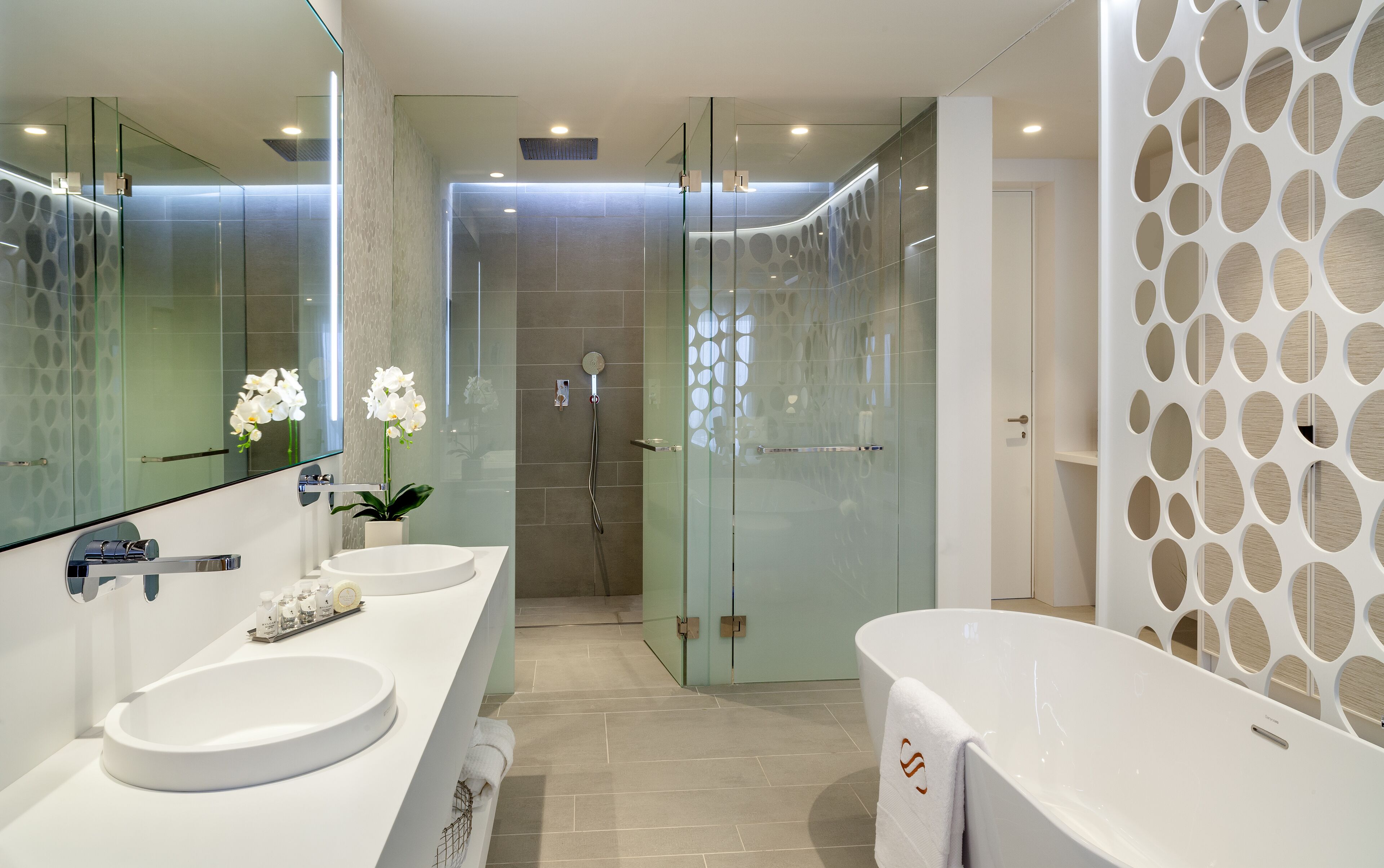 A modern bathroom with two sinks, a glass shower enclosure, and a decorative wall panel.