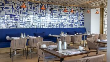 Un café moderno con mobiliario de mimbre, cojines azules y una pared con estampado.