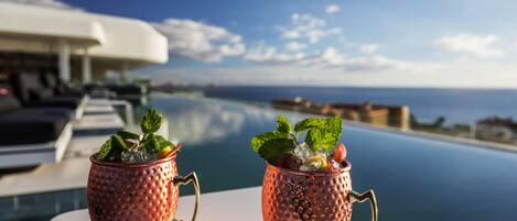 Two copper mugs with handles on a white table by a poolside, overlooking the sea.